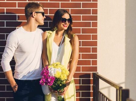 Young fashion couple posing on the old street in sunny spring. Pretty beautiful woman with yellow flowers and her handsome boyfriend hugging on the street. Couple in love dating. Romantic mood.