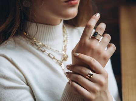 closeup of a woman in a cream turtleneck sweater wearing a gold necklace and two gold rings