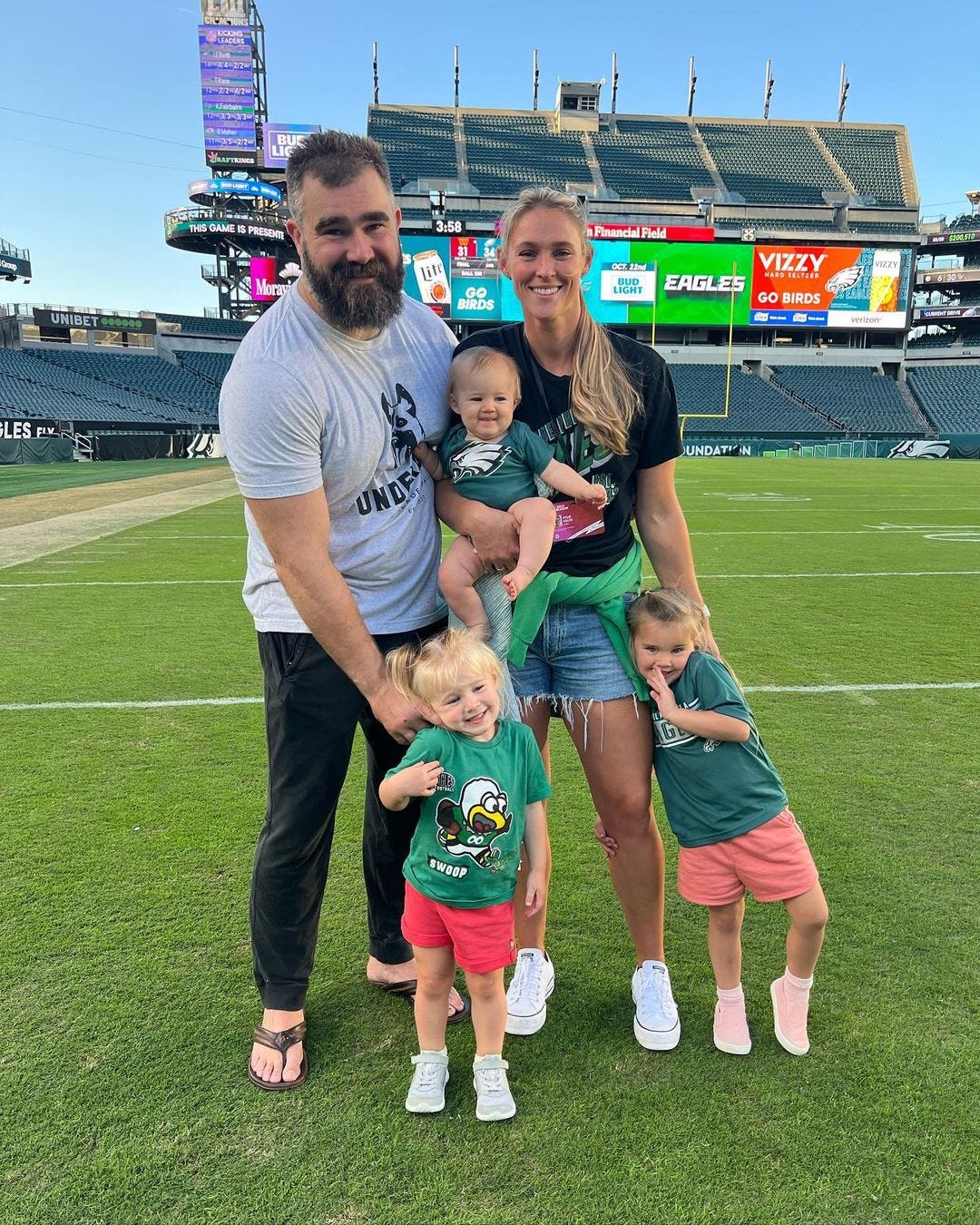 Jason Kelce on football field with wife and three daughters in Philadelphia Eagles gear