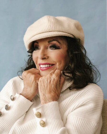 Joan Collins rests her chin on her fists as she smiles. Her dark hair flows out of her cream-colored beret. She wears a matching sweater and pink lipstick.