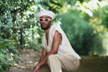 man squatting down wearing a beret, white glasses and a sweater vest