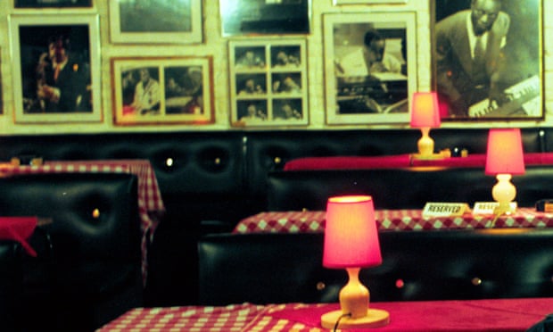 An old-fashioned bar with checked tablecloths, lamps on the tables and photos on the walls