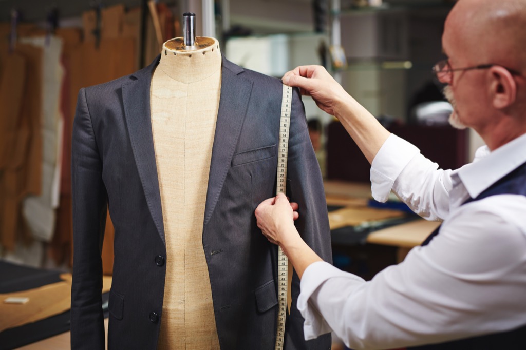 tailor measuring a men's suit jacket on a mannequin