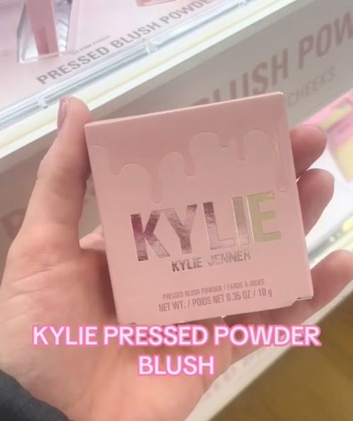 Still from a video of a woman holding up makeup products in a store