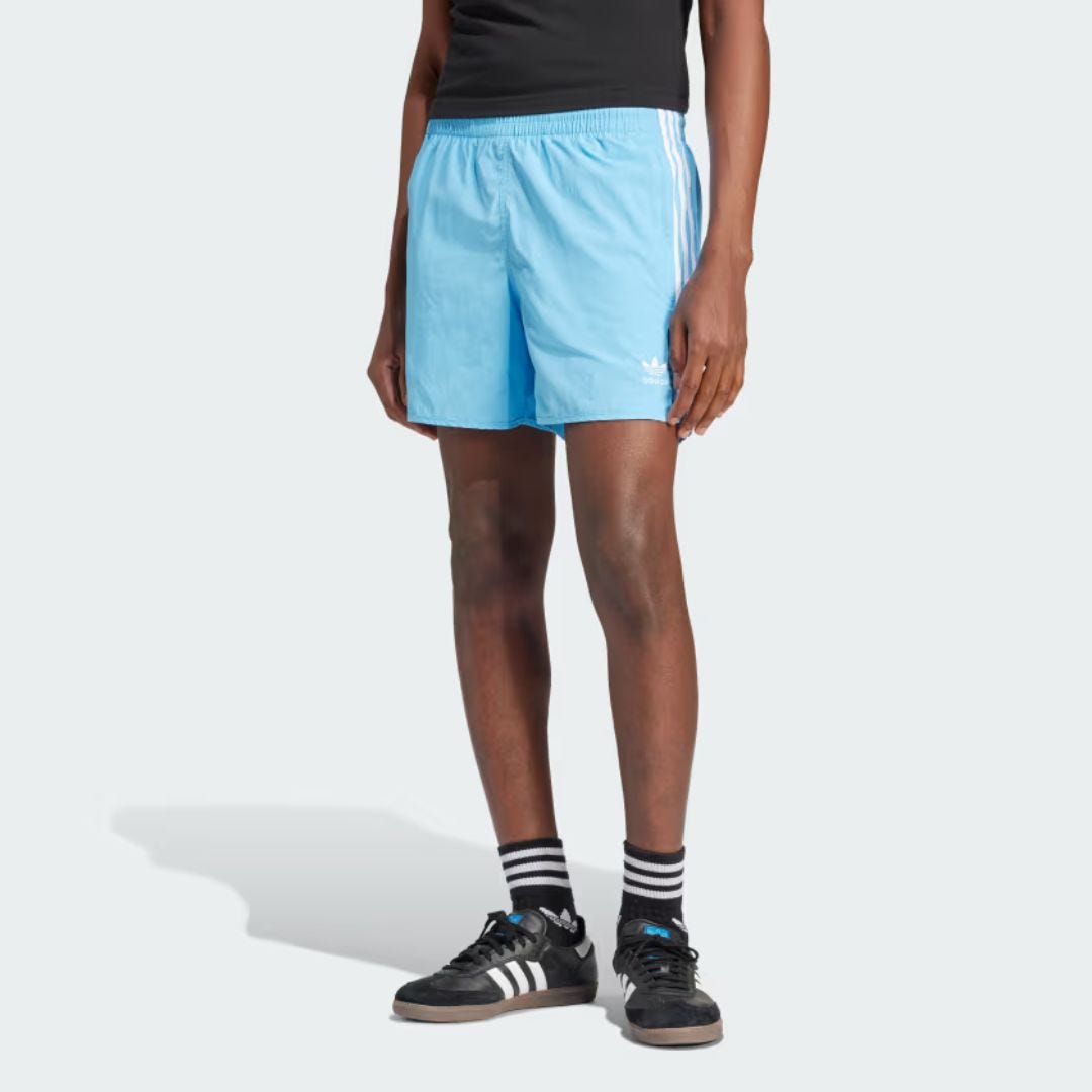 lower half of a man wearing light blue adidas soccer shorts and samba sneakers