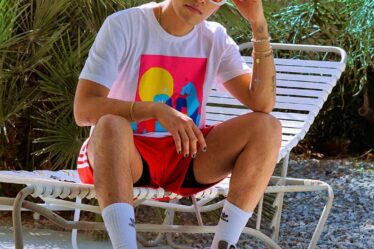 young man in a white t-shirt and red adidas shorts sitting on a pool chair