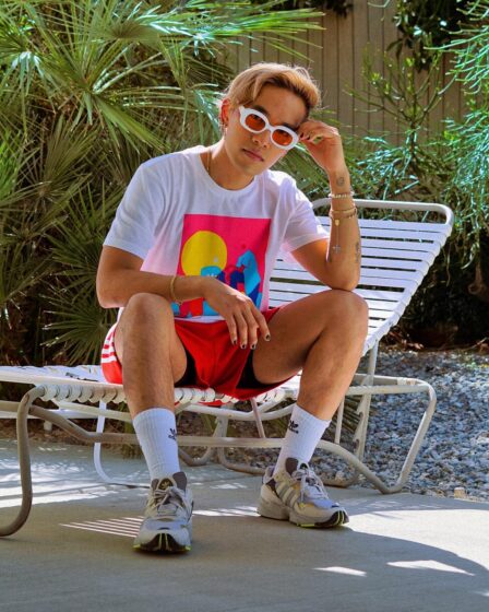 young man in a white t-shirt and red adidas shorts sitting on a pool chair