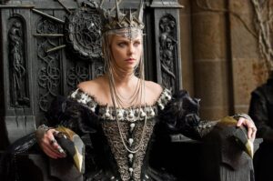 Charlize Theron playing a wicked queen in the film Snow White and the Huntsman sitting upon a throne wearing a crown.