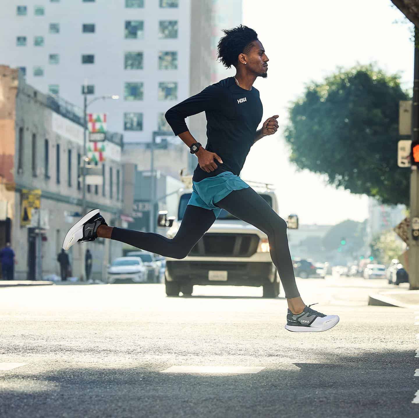 man running on the street wearing a pair of transport sneakers by hoka