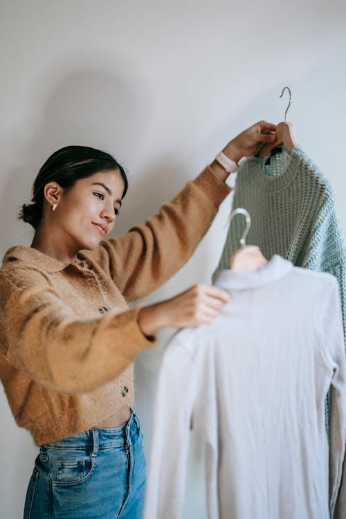 Free Happy young woman choosing pullovers on hangers Stock Photo