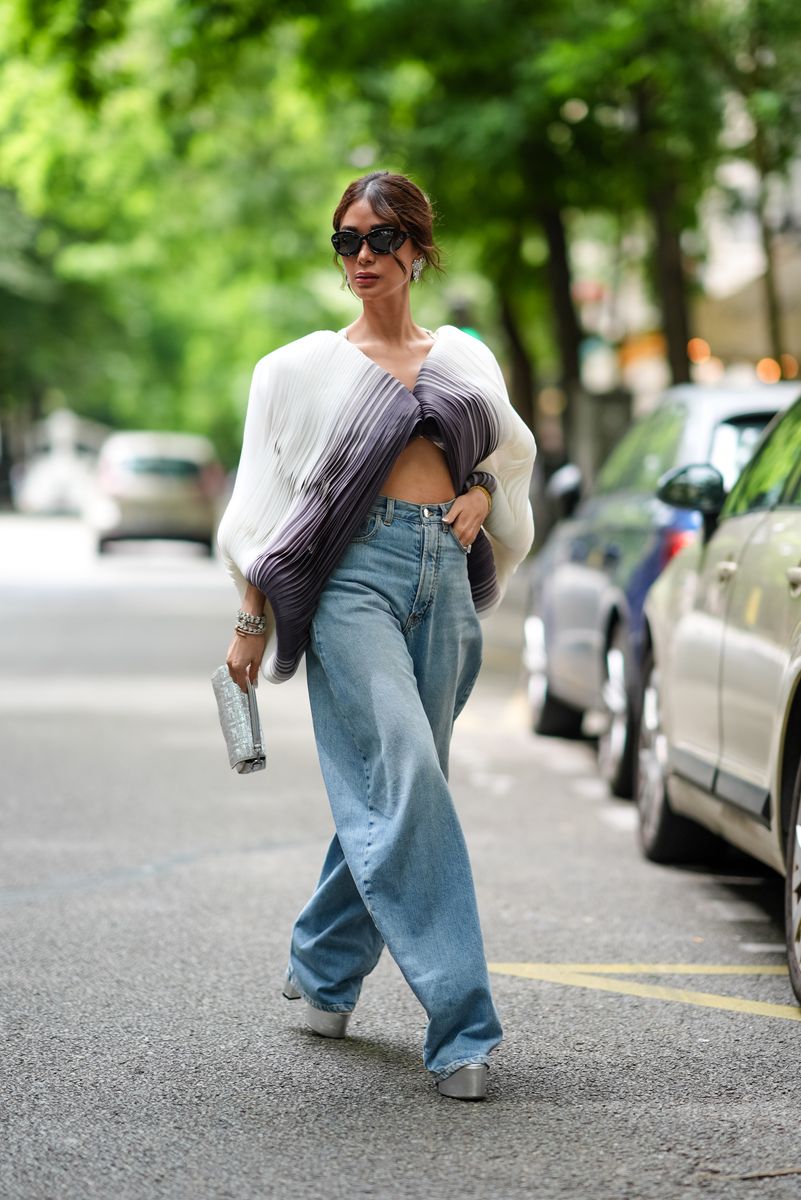 Heart Evangelista wears black sunglasses, silver diamond earrings, a white and purple layered/pattern cropped v-neck flowy long-sleeve shirt, a silver diamond bracelet, a Cartier bracelet, a silver and white sparkly Fendi bag, light blue baggy loose denim jean pants, and silver metallic platform heels outside BlueMarble on June 20, 2024, during the Paris Fashion Week Menswear Spring/Summer 2025 in Paris, France.