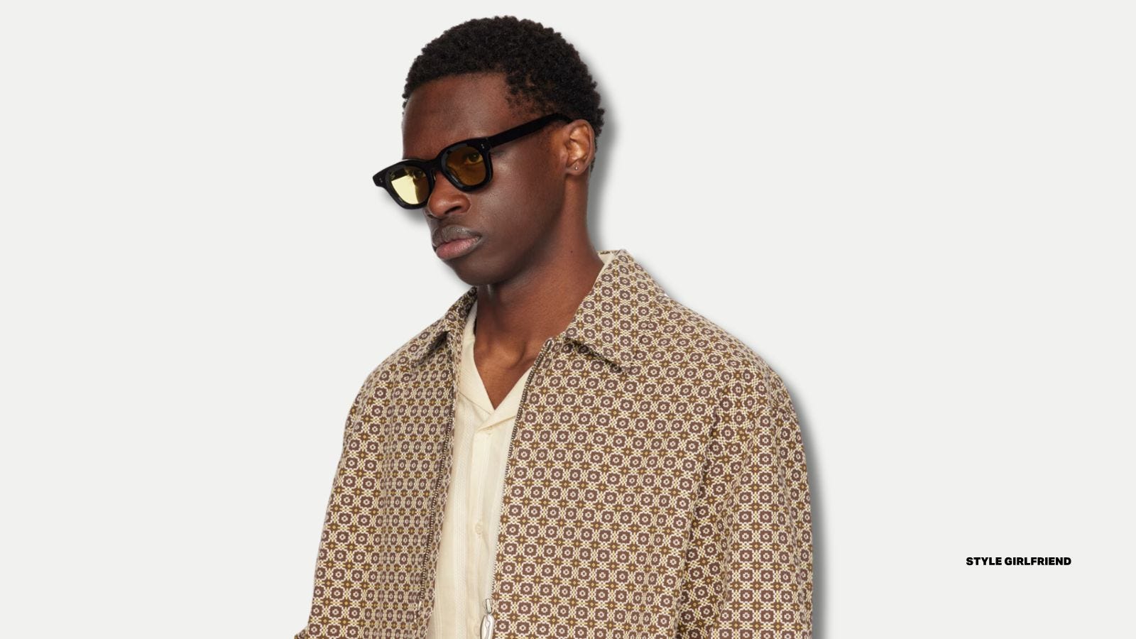 man wearing yellow lens sunglasses and a brown patterned coat over a v-neck shirt