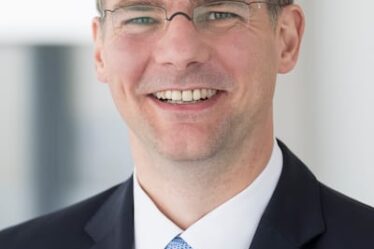 Headshot of Dr. Stefan Droste wearing a navy suit, white shirt and blue tie.