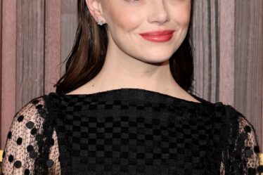 Emma Stone poses at a premiere in a black dress. Her hair is a dark brown with red undertones.