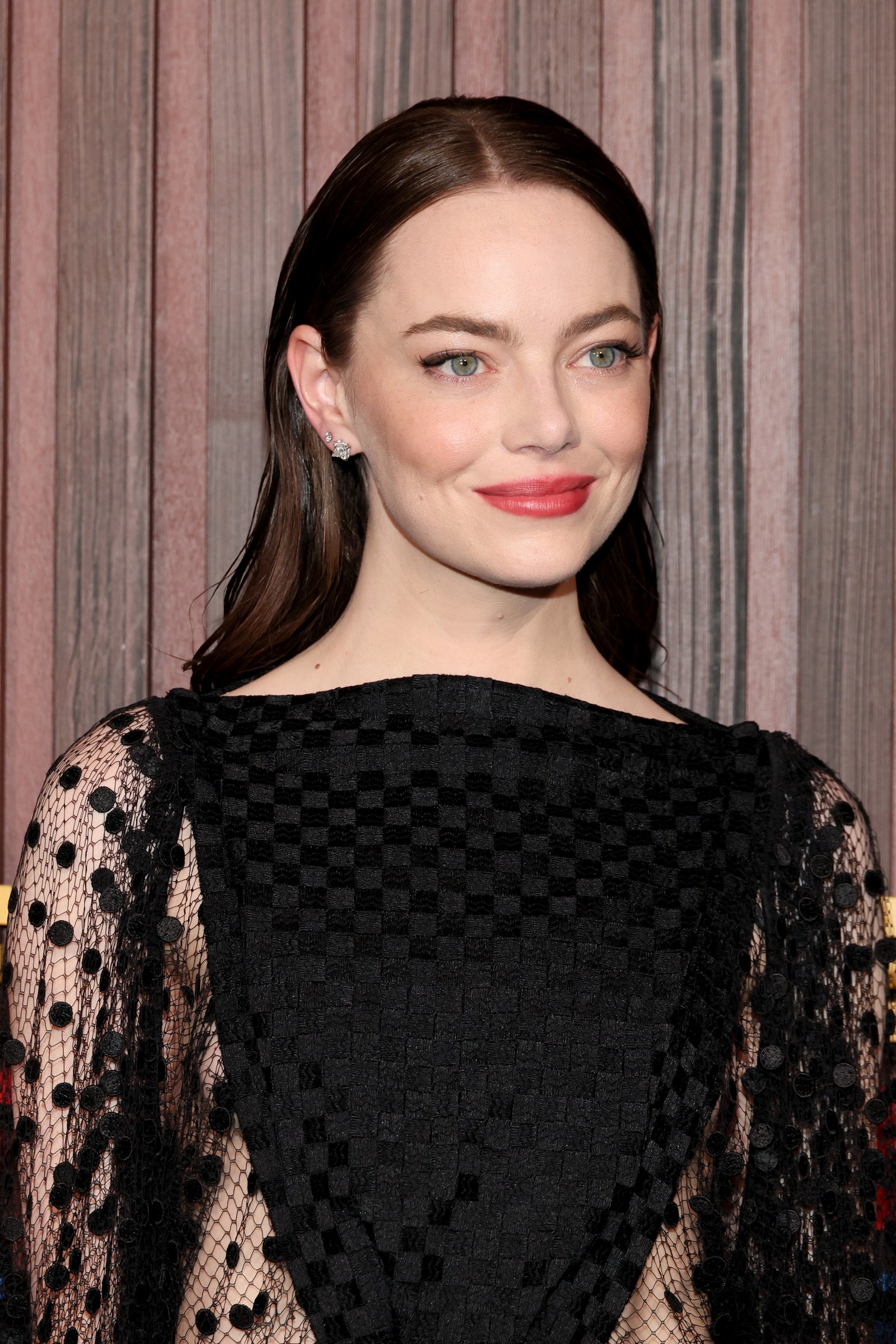 Emma Stone poses at a premiere in a black dress. Her hair is a dark brown with red undertones.