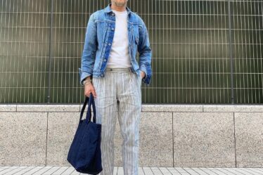 man in a denim jacket, white t-shirt, and striped pants, holding a navy bag