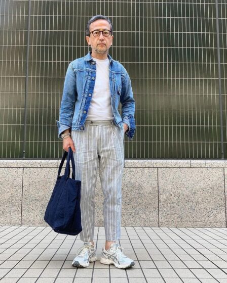 man in a denim jacket, white t-shirt, and striped pants, holding a navy bag