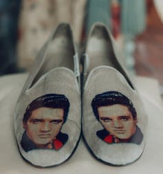 A pair of grey velvet slippers with Elvis on them.