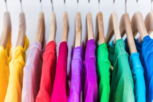 Fashion clothes on clothing rack - bright colorful closet. Closeup of rainbow color choice of trendy female wear on hangers in store closet or spring cleaning concept. Summer home wardrobe.