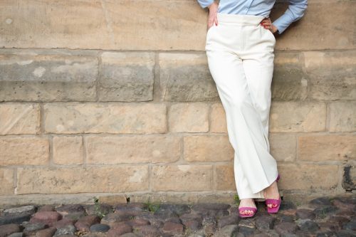 a successful young woman in white trousers and a blue shirt. the woman is leaning against the wall. A shortened shot of a woman's legs in classic trousers. copy space