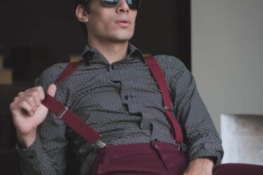 man with sunglasses sitting on a chair wearing maroon suspenders