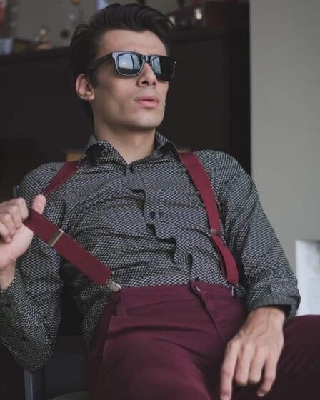 man with sunglasses sitting on a chair wearing maroon suspenders