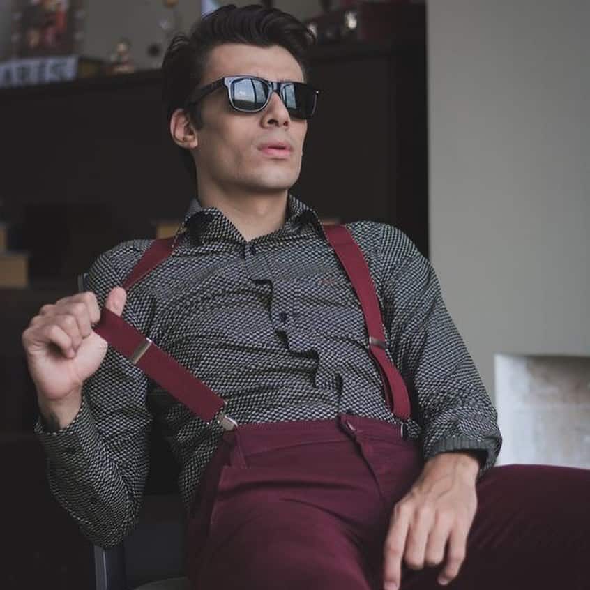 man with sunglasses sitting on a chair wearing maroon suspenders