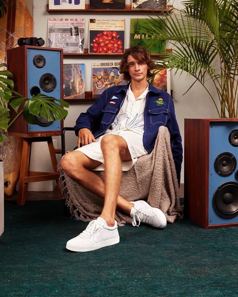 man sitting on a chair wearing a pair of white sneakers by cariuma