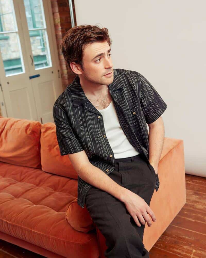 man sitting on a sofa's arm wearing an unbuttoned cuban shirt