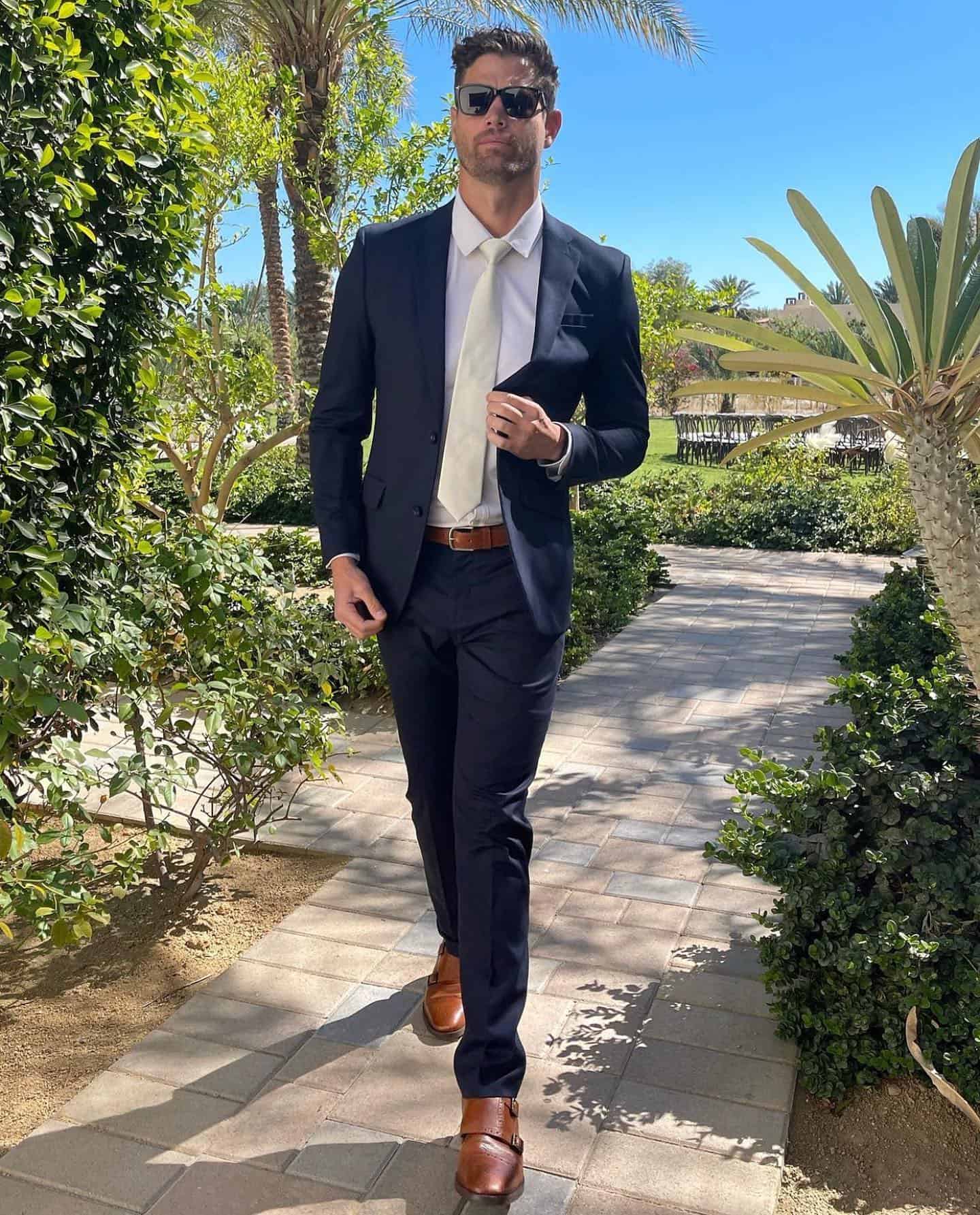 man wearing a navy suit with brown belt and brown shoes