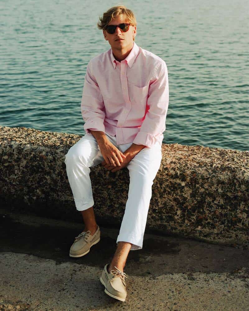 man sitting on a seawall wearing pink shirt and white pants