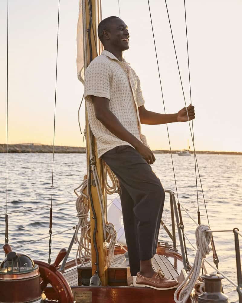 man standing on a boat wearing a shirt and linen pants