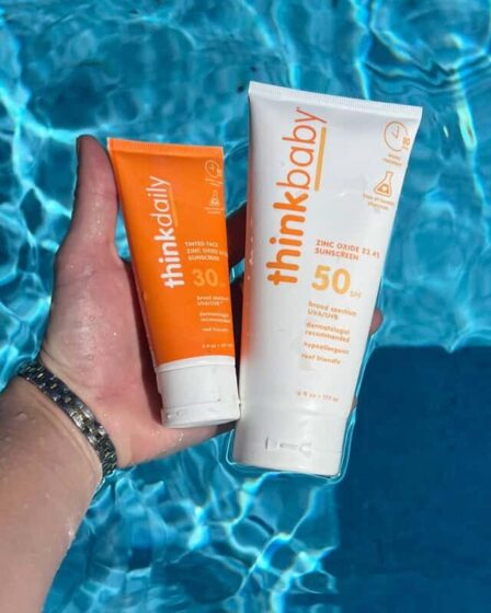 holding bottles of thinkdaily and thinkbaby sunscreen with zinc oxide