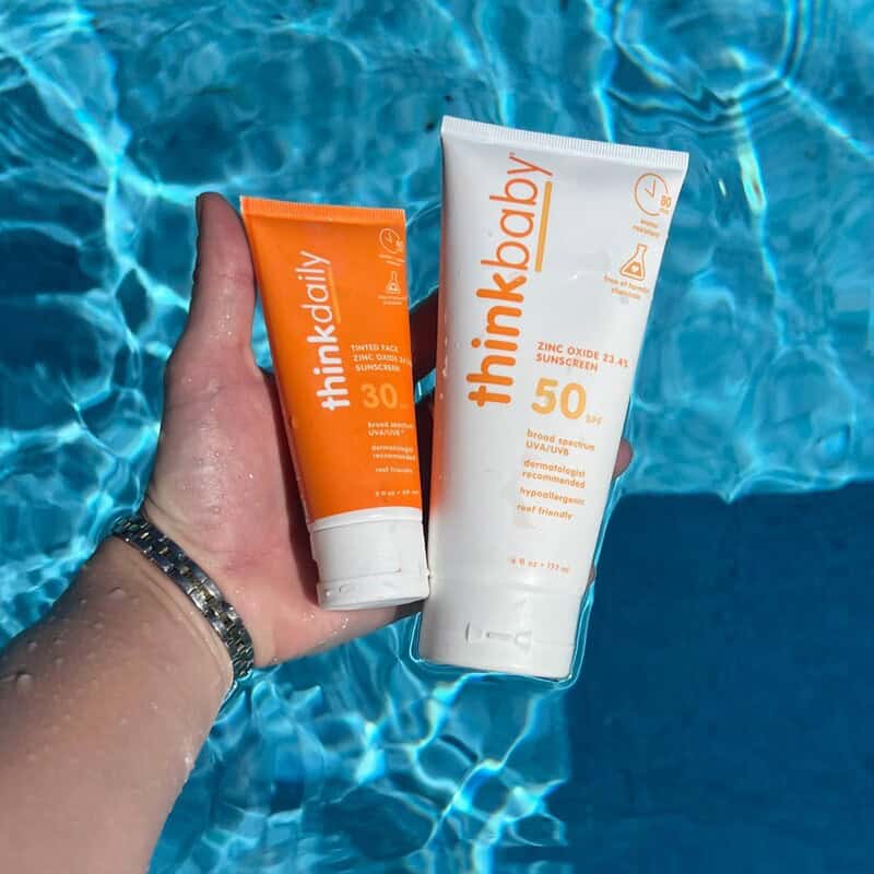 holding bottles of thinkdaily and thinkbaby sunscreen with zinc oxide