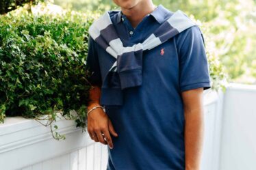 man wearing a navy blue polo shirt with sweater tied around the shoulders