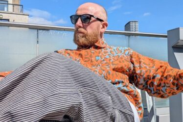 man seated in an orange animal print shirt with train conductor stripe pants