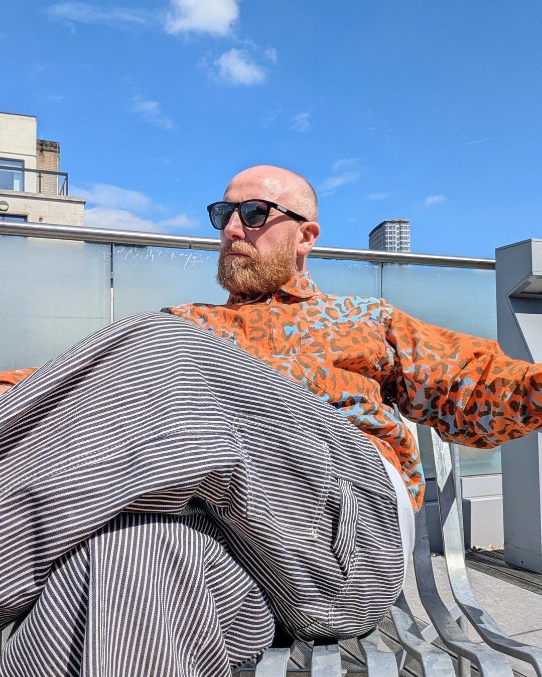 man seated in an orange animal print shirt with train conductor stripe pants