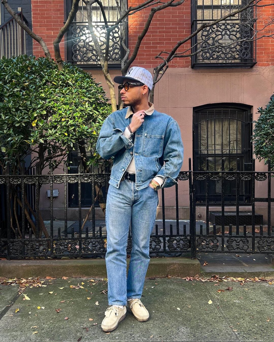 young man standing on the sidewalk wearing a light denim jacket with corduroy collar and light wash jeans