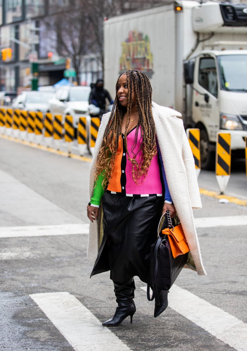 NEW YORK, NEW YORK - FEBRUARY 16: A guest is seen wearing multi colored button up top, black leather skirt, white coat, orange black bag, knee high boots outside Collina Strada during New York Fashion Week on February 16, 2022 in New York City. (Photo by 