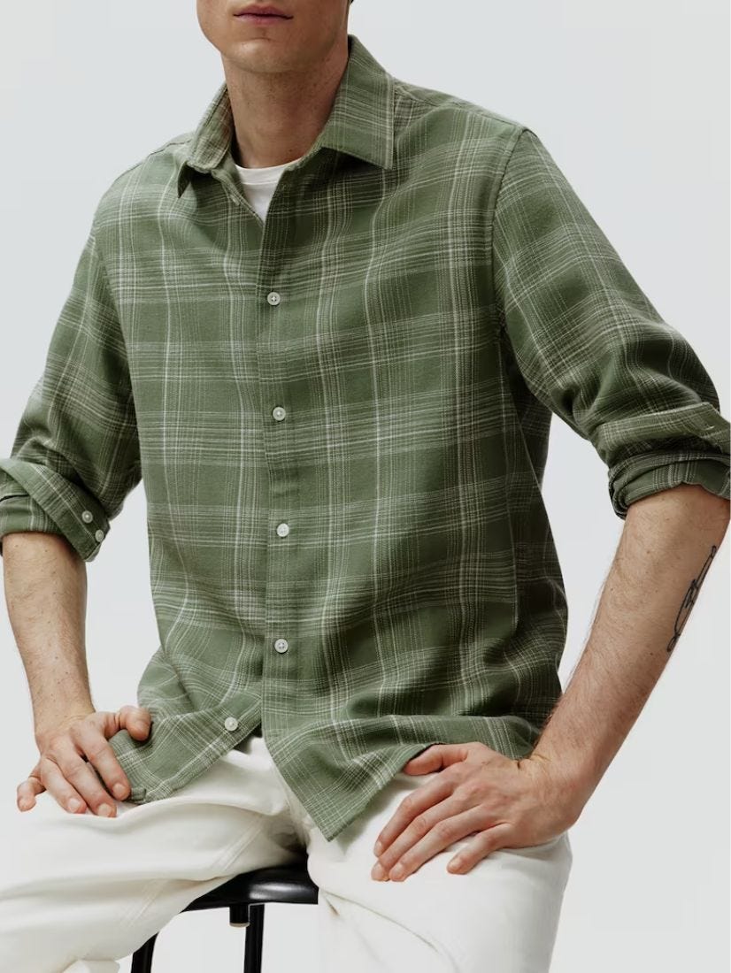 close-up of a man from the waist up sitting on a stool wearing a green flannel shirt