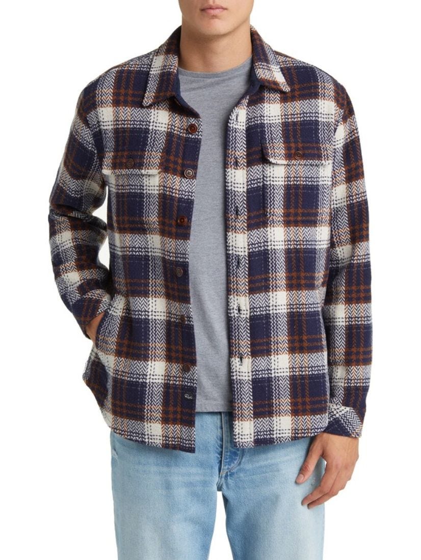 close-up of a man wearing a burgundy and navy plaid flannel shirt over a grey t-shirt and light blue jeans