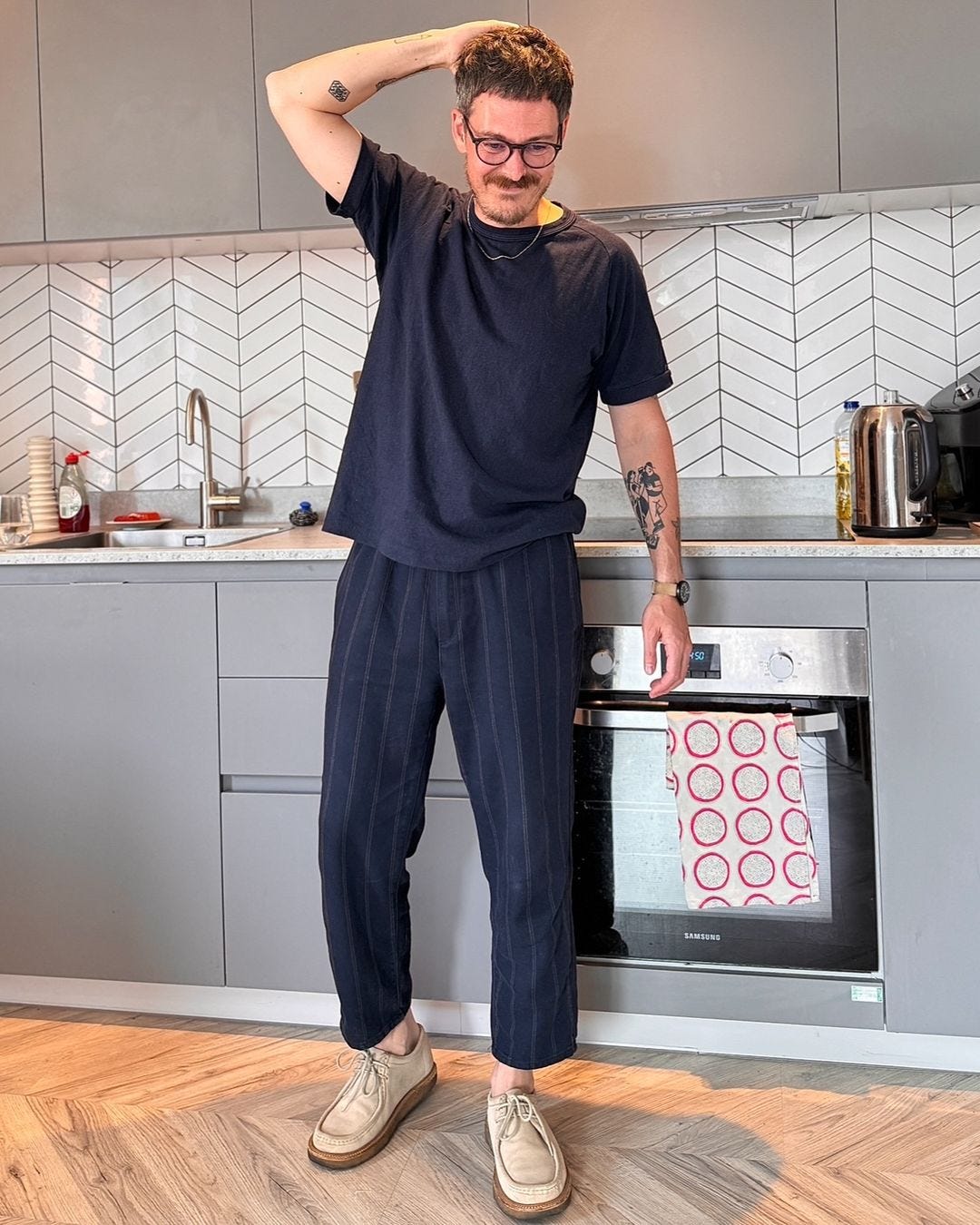 man standing in a kitchen wearing dark striped pants and a coordinating t-shirt