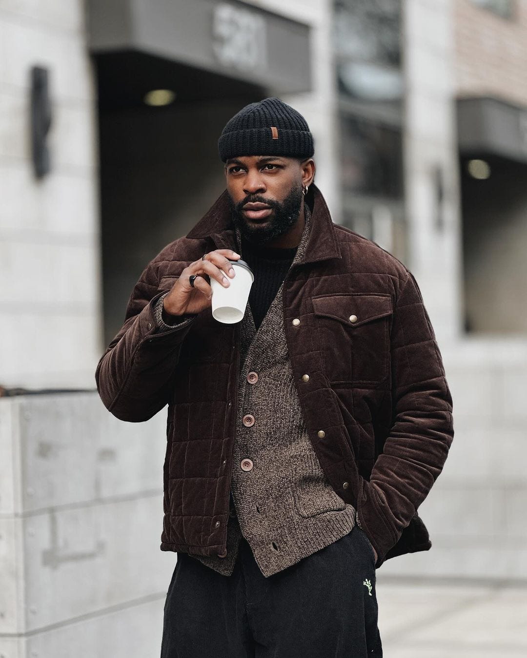 man wearing a chocolate-brown puffer jacket over a marled brown cardigan