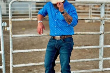 man in a blue shirt and jeans tilting down his cowboy hat