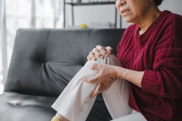 Elderly housewife woman sitting on sofa. knee pain