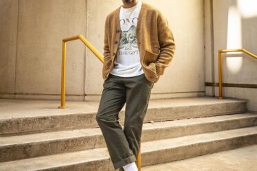 man standing in front of stairs wearing a mustard-colored cardigan, white t-shirt, olive pants, and Nike high top sneakers