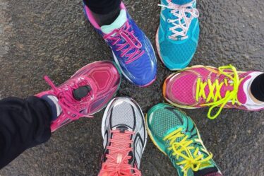 Overhead view of 6 brighlty colored runners' shoes on wet pavement