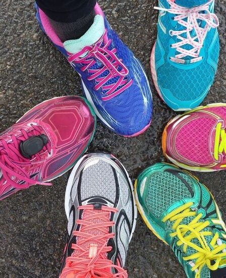 Overhead view of 6 brighlty colored runners' shoes on wet pavement