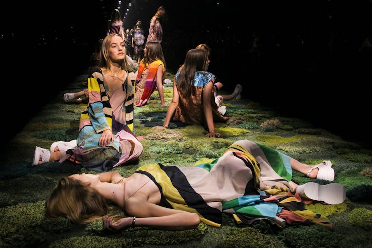 A group of models lying on the catwalk at the end of a show.