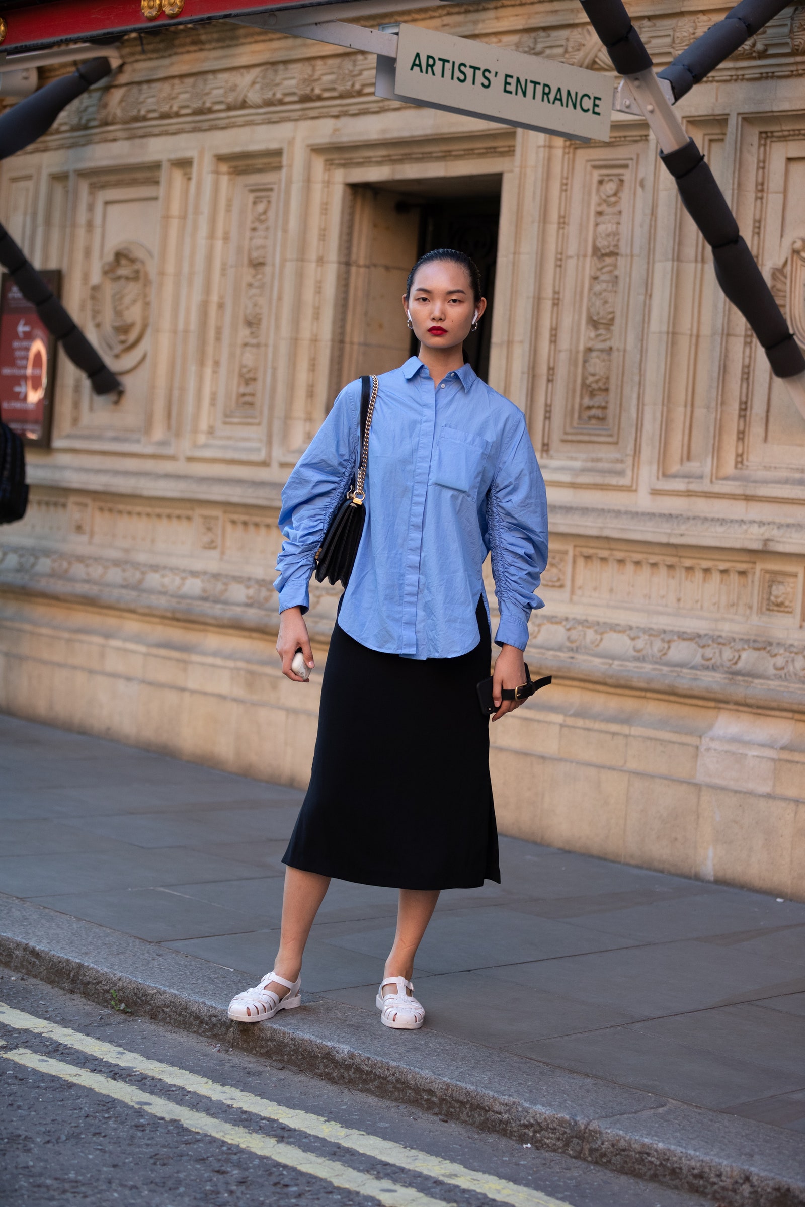 LONDON ENGLAND  SEPTEMBER 15 Model Ling Chen wears Airpods a blue blouse black skirt and light pink jelly sandals after...